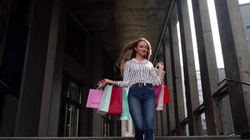 sorridente ragazza a piedi a partire dal centro centro commerciale con shopping borse, contento con Acquista su nero Venerdì video