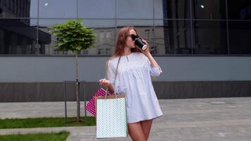 Girl stay near mall with shopping bags and drinking coffee. Relaxing after shopping in fashion store video