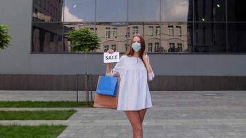 ragazza nel protettivo maschera con shopping borse mostrando vendita parola iscrizione durante covid-19 pandemia video