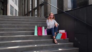 menina sentado em escadas com bolsas falando em Móvel telefone sobre venda dentro compras Shopping dentro Preto Sexta-feira video