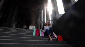 Teenager smiling girl with shopping bags sitting on stairs near shopping mall. Black Friday sale video