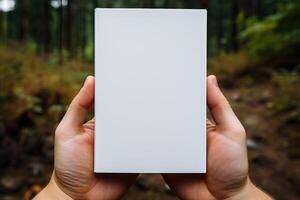 A man holds a sheet of A4 format in his hands on a forest background. photo