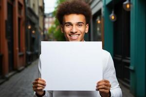 A guy of African appearance holds in his hands a white blank sheet of paper with a place for writing or mockup. A person with a white banner on the street. photo