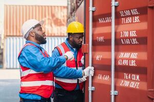 Portrait of Two African Engineer or foreman wears PPE checking container storage with cargo container background at sunset. Logistics global import or export shipping industrial concept. photo