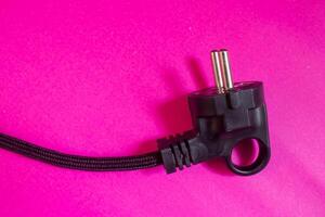 Black electric plug isolated on pink background. Top view, copy space. photo