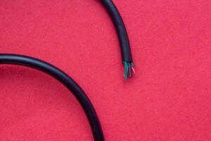 Damaged electrical cable isolated on red background, closeup photo