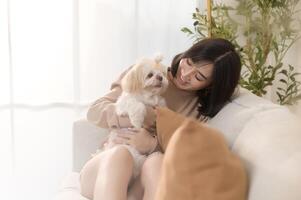 Happy young asian woman cuddling and spending time with cute dog in living room. photo