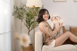 Happy young asian woman cuddling and spending time with cute dog in living room. photo