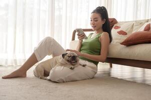 Happy young asian woman cuddling and spending time with cute dog in living room. photo