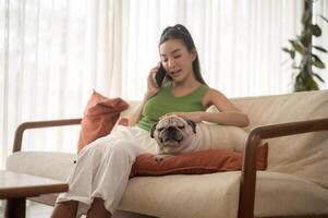 Happy young asian woman cuddling and spending time with cute dog in living room. photo