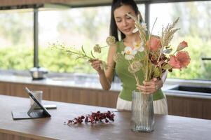 Asian smiling woman putting beautiful flowers on jar , enjoying decorating at home photo