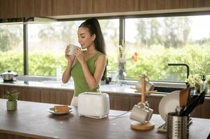 asiático mujer preparando café y brindis un pan para desayuno a el cocina mesa en el Mañana foto