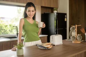 asiático mujer preparando café y brindis un pan para desayuno a el cocina mesa en el Mañana foto