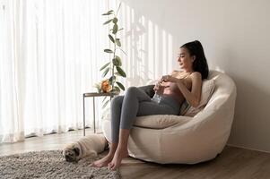 Young asian woman in sportswear drinking pure water from glass in living room at home photo