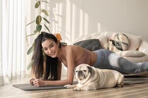 asiático mujer en ropa de deporte hacer ejercicio y haciendo yoga con linda perro en vivo habitación a hogar, sano estilo de vida, mental salud concepto. foto