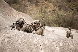 Soldiers in camouflage uniforms aiming with their riflesready to fire during military operation in the desert soldiers training  in a military operation photo