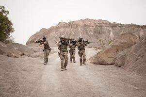 Soldiers in camouflage uniforms aiming with their riflesready to fire during military operation in the desert soldiers training  in a military operation photo