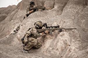 Soldiers in camouflage uniforms aiming with their riflesready to fire during military operation in the desert soldiers training  in a military operation photo