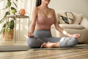 asiático mujer en ropa de deporte hacer ejercicio y haciendo yoga en vivo habitación a hogar, sano estilo de vida, mental salud concepto. foto