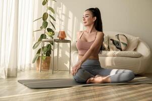 asiático mujer en ropa de deporte hacer ejercicio y haciendo yoga en vivo habitación a hogar, sano estilo de vida, mental salud concepto. foto