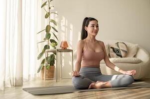 asiático mujer en ropa de deporte hacer ejercicio y haciendo yoga en vivo habitación a hogar, sano estilo de vida, mental salud concepto. foto