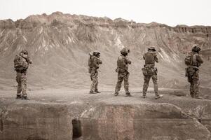 Soldiers in camouflage uniforms aiming with their riflesready to fire during military operation in the desert soldiers training in a military operation photo