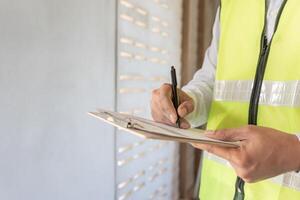 el inspector o ingeniero está inspeccionando la construcción y el aseguramiento de la calidad de la nueva casa usando una lista de verificación. ingenieros o arquitectos o contratistas trabajan para construir la casa antes de entregársela al propietario foto