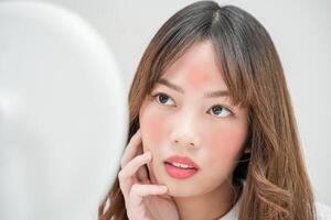 joven mujer asiático son preocupado acerca de caras dermatología y alérgico a esteroides en productos cosméticos. sensible piel, rojo cara desde bronceado, acné, alérgico a quimicos, erupción en rostro. piel problemas y belleza foto