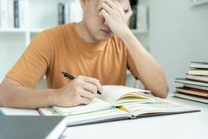 el estudiante asiático tiene ansiedad debido a los exámenes, los hombres se preparan para el examen y aprenden lecciones en la biblioteca. estrés, desesperación, prisa, malentendido lectura, desanimado, expectativa, conocimiento, cansado foto