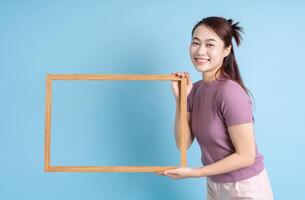 Young Asian woman holding photo frame on blue background