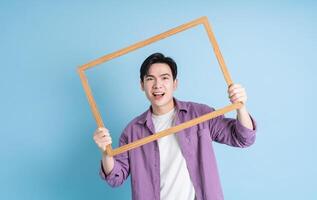 Young Asian man holding photo frame on blue background