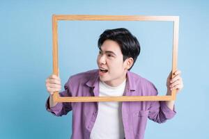 joven asiático hombre participación foto marco en azul antecedentes