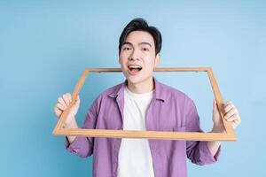 Young Asian man holding photo frame on blue background