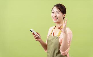 Photo of young Asian female housekeeper on green background