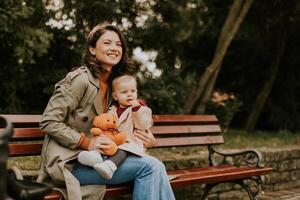 Young woman sitting on a bench with cute baby girl in the autumn park photo