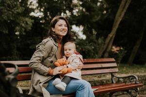 Young woman sitting on a bench with cute baby girl in the autumn park photo