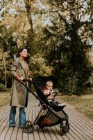 Young woman with cute baby girl in baby stroller at the autumn park photo