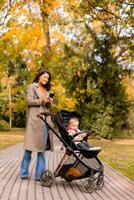 Young woman with cute baby girl in baby stroller using mobile phone at the autumn park photo
