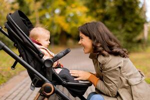 Young woman with cute baby girl in baby stroller at the autumn park photo