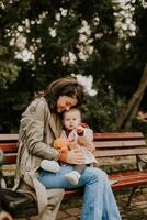 Young woman sitting on a bench with cute baby girl in the autumn park photo