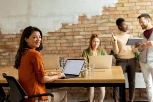 Business woman working on laptop with her young multiethnic startup team in the modern office photo