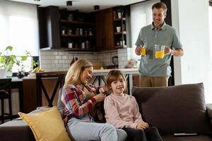 Smiling father brings a tray of orange juice to his happy family seated in a living room photo