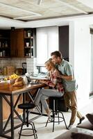 Cheerful couple enjoys a light-hearted moment in their sunny kitchen, working on laptop surrounded by a healthy breakfast photo