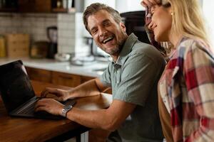 Cheerful couple enjoys a light-hearted moment in their sunny kitchen, working on laptop surrounded by a healthy breakfast photo