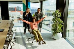 Jubilant Office Celebration Captures Colleagues Spontaneous Chair Race in Sunlit Room photo