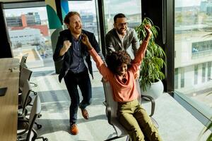 Jubilant Office Celebration Captures Colleagues Spontaneous Chair Race in Sunlit Room photo