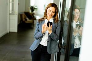 Smiling Businesswoman in Modern Office Holding Smartphone Enjoying a Successful Work Day photo