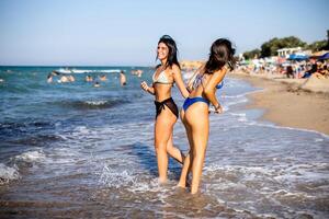 dos bonito joven mujer teniendo divertido en el playa foto