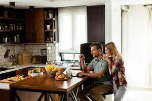 Cheerful couple enjoys a light-hearted moment in their sunny kitchen, working on laptop surrounded by a healthy breakfast photo