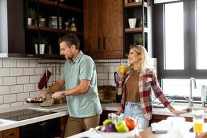 Man and woman sharing a laugh as they cook in a cozy, well-organized kitchen photo